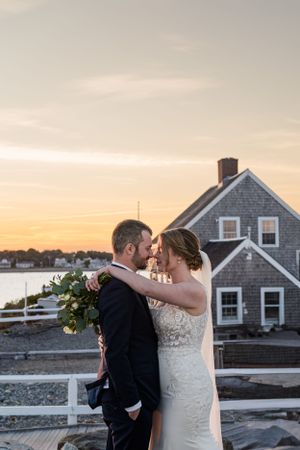 A romantic sunset moment at a coastal New England wedding with a shingle-style house in view.