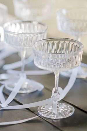 Vintage cut crystal champagne coupe glasses with white ribbons on display.
