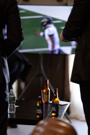 Beer bottles and water on a table with a sports game playing on TV in the background.