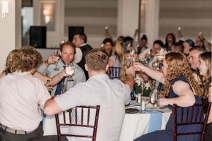 Wedding reception guests raising glasses in a celebratory toast at decorated tables.
