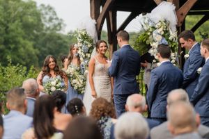 Outdoor wedding ceremony surrounded by guests under a rustic wooden structure.
