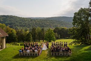 Panoramic mountain view of an outdoor wedding ceremony setup with white chairs on a lush green lawn.