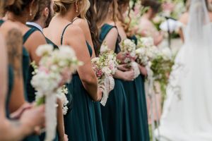Bridesmaids in teal dresses holding white floral bouquets stand together at an elegant wedding ceremony.