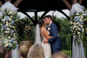 Couple shares their first kiss as newlyweds under floral-decorated wooden arch.