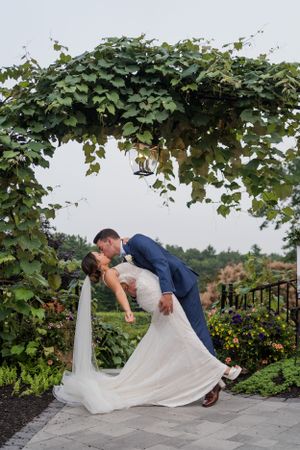 Romantic dip kiss under an ivy-covered archway in a garden setting.