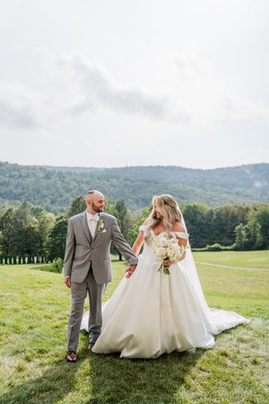 Wedding couple poses together on a scenic hilltop meadow with mountain views in the background.
