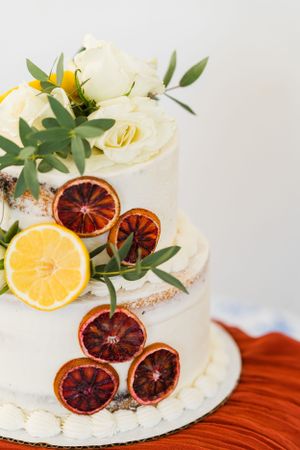 A white frosted wedding cake decorated with citrus slices and greenery on rustic wooden surface.
