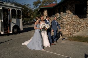 Wedding party walking together on a stone pathway outside a rustic venue with arched architecture.