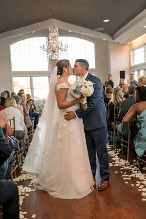 A couple sharing romantic kisses during their wedding ceremony in an elegant venue with scattered rose petals.