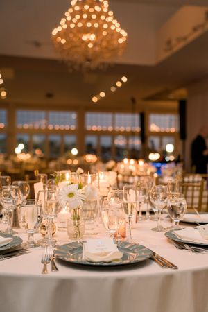 Elegant wedding reception tables set with glassware and warm lighting from overhead chandeliers.