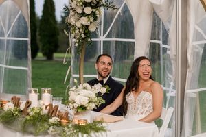 Newlyweds share a joyful moment at their reception table decorated with white floral arrangements and candles.
