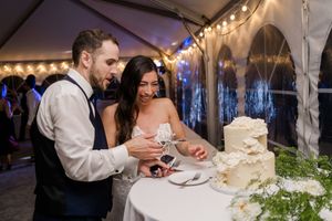 Newlyweds cut into their elegant white wedding cake during the reception celebration under twinkling lights.