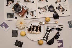 Vintage camera, sunglasses, and macarons arranged with polaroid photos and a white flower on a flat surface.