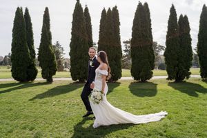Wedding couple poses on a lawn with tall cypress trees creating an elegant outdoor backdrop.
