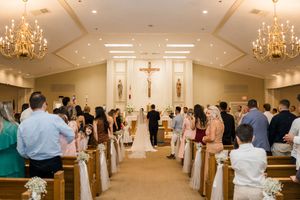 A traditional Catholic wedding ceremony takes place in a chapel with ornate chandeliers and white decor.
