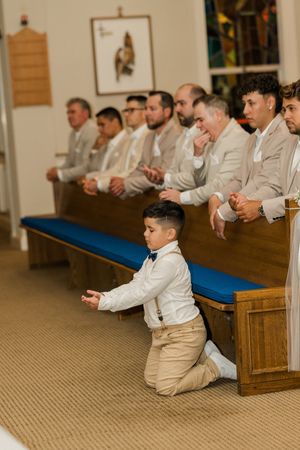 A group sits in church pews during a ceremony wearing light colored formal attire.