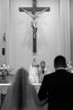 Black and white photo of a religious ceremony in a church with crucifixes and candles visible in the background.
