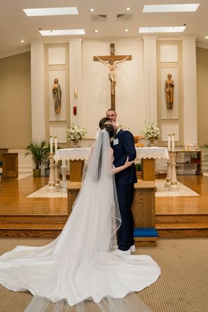 A wedding couple embraces in a beautiful church sanctuary with a long flowing white veil trailing behind them.