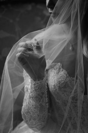 A black and white close-up of delicate lace wedding dress details with flowing veil.