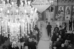 Elegant crystal chandeliers illuminate a grand ballroom during a traditional wedding ceremony with guests seated.