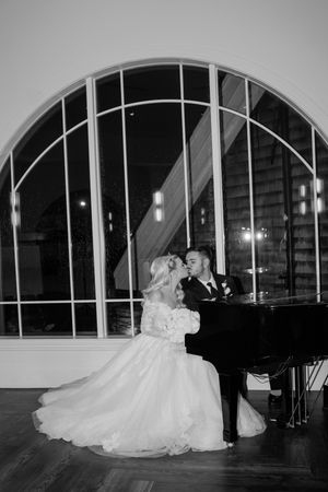 Black and white photo of a couple dancing in an elegant venue with arched windows at night.