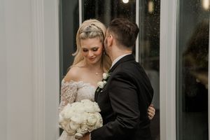 A bride and groom share an intimate moment in front of glass windows at their elegant evening wedding reception.