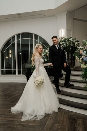 A romantic first dance sequence between newlyweds in a beautiful white ballroom with arched windows and floral decor.