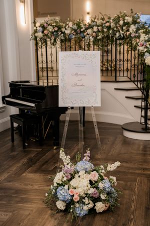 Wedding ceremony setup with floral arrangements, signage and a grand piano in an elegant white room.