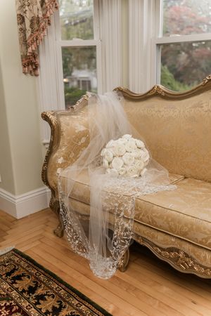 A vintage gold damask sofa with a delicate white lace veil and rose bouquet draped across it.