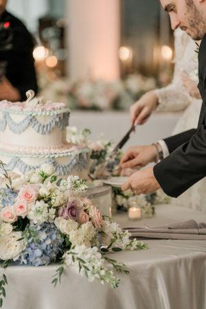 A wedding cake cutting scene with delicate floral arrangements of roses and hydrangeas on an elegant table setting.