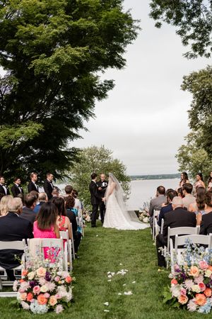 Outdoor wedding ceremony overlooking a lake with floral arrangements and white chairs on a grassy lawn.