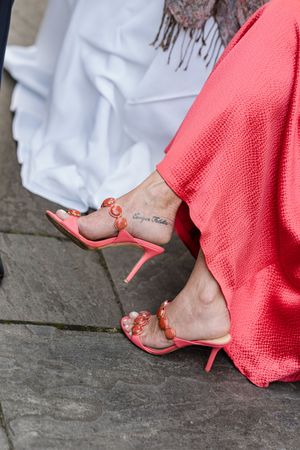 Coral pink shoes with delicate straps shown against a stone surface.
