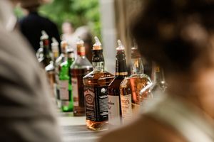 Various liquor bottles lined up on a dark wooden bar in soft focus.