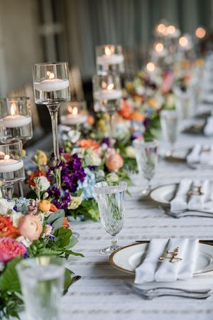 Elegant wedding reception table settings with candlelit centerpieces, white linens, and colorful floral arrangements.