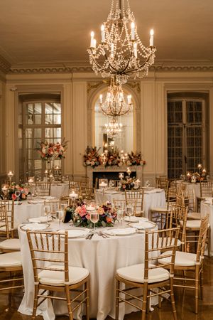 Elegant ballroom with crystal chandeliers and gold chairs set for a wedding reception.