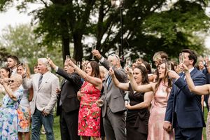 Wedding guests stand in a line outdoors clapping and celebrating during a joyful outdoor ceremony.