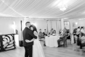 Black and white motion shot of first dance in an elegant reception venue with draped ceiling.