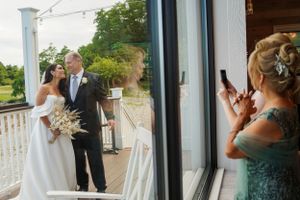 Wedding party member taking photo of couple through glass door.