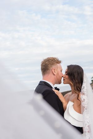 Romantic moment between newlyweds against cloudy sky background.
