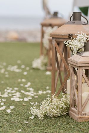 Rustic wooden lanterns decorated with baby's breath flowers along a grassy path during an outdoor event.