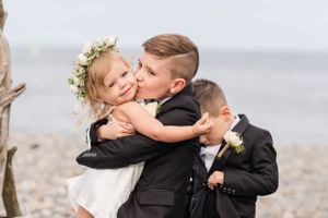 Sweet moment captured between young children in formal attire on a beach during a wedding celebration.