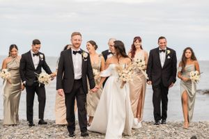 Wedding party in formal attire and neutral colors walking along a beach at sunset.