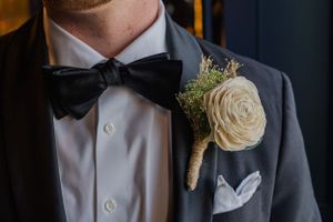 Close-up of groom's formal attire with white rose boutonniere and black bow tie.