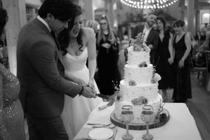 A wedding couple cuts their elegant white tiered cake under chandelier lighting.