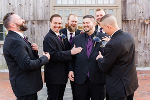 Wedding party members sharing a joyful moment together outside a barn.