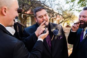 Groomsmen sharing cigars and laughing together before the wedding ceremony.