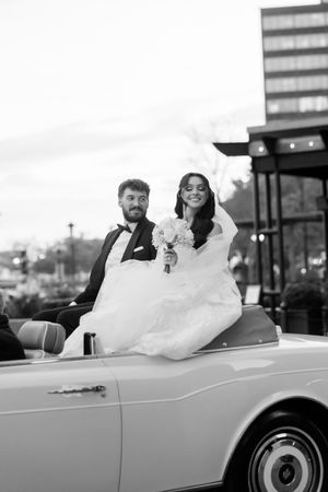 A classic white convertible car decorated for a wedding celebration with flowing white fabric.