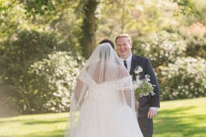 A couple shares a romantic moment in a sunlit garden with a flowing white wedding dress catching the breeze.