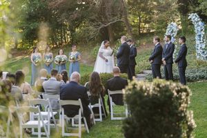 A beautiful outdoor wedding ceremony takes place in a lush garden setting with white chairs arranged on the grass.