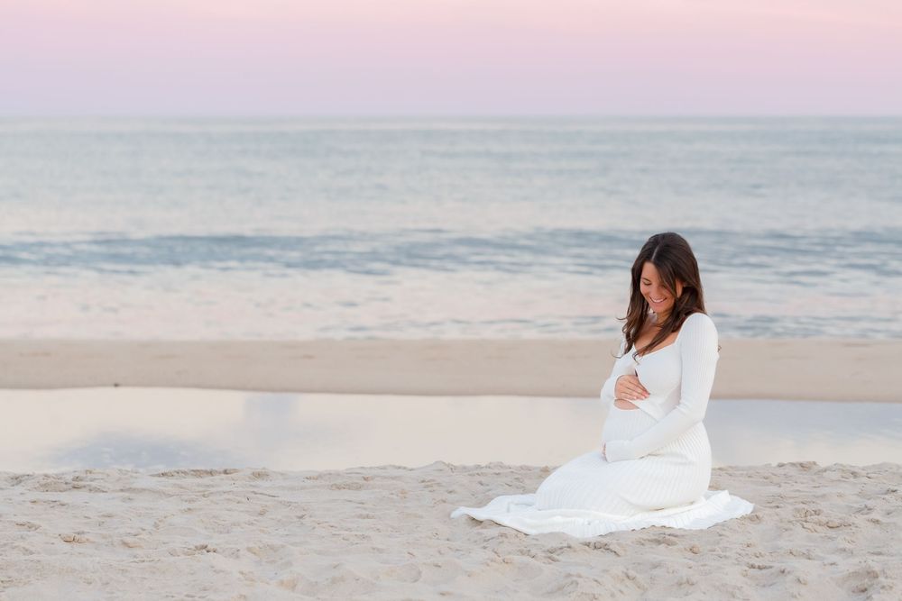 A person in a flowing white dress poses gracefully on a sandy beach at sunset.